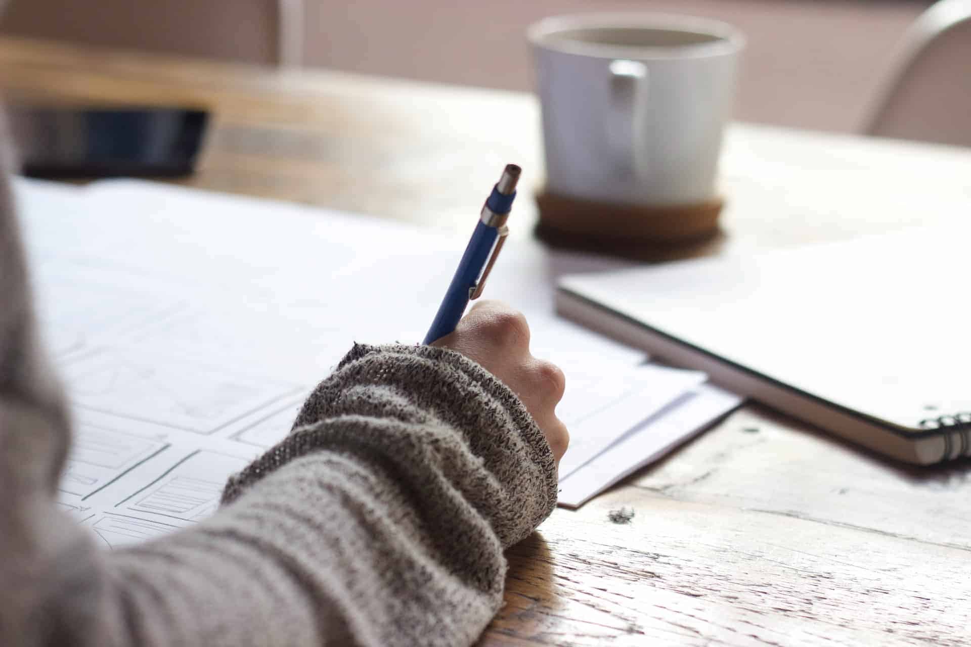 A person's hand holding a pen over a notepad, brainstorming content reuse strategies, with a cozy sweater sleeve visible, symbolizing the creative process behind Wild Wattle Digital's blog post '5 Clever Ways to Reuse Your Content'